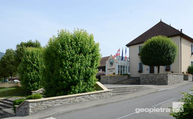 Anthon town hall with Geopietra reconstituted stone walls, national flags displayed, and well-maintained trees in the front courtyard.